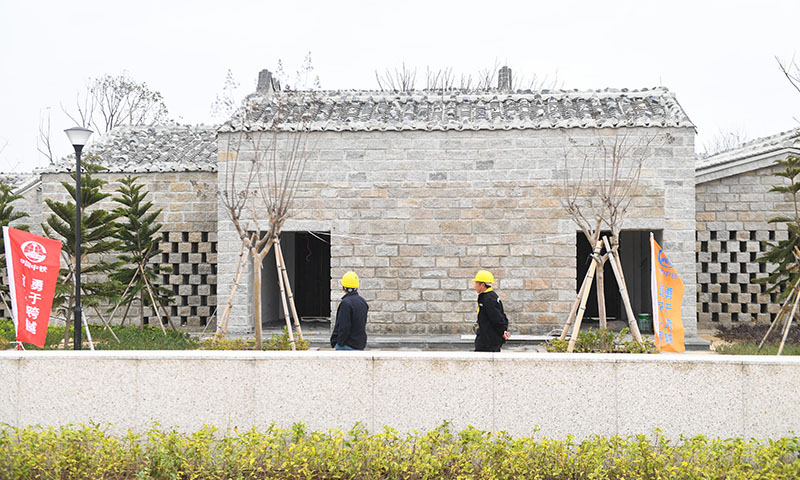 福平鐵路平潭一體化綜合交通樞紐由中鐵一局承建，匯集高鐵、公交、出租車、網約車、私家車等多種交通出行模式，為旅客提供“零換乘”和“無縫銜接”體驗。該交通樞紐采用“石頭厝”傳統民居形式，將平潭地方建筑特征與現代建筑功能相結合，合理運用自然采光和空氣通風原理。圖為12月7日，中鐵一局工人從福平鐵路平潭一體化綜合交通樞紐站前廣場“石頭厝”傳統建筑前經過。（新華社記者 宋為偉 攝）