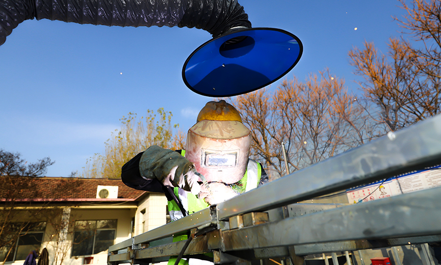 在施工過程中，項目綜合以往施工經驗結合施工工期，決定大膽采用裝配式安裝思路。首先建立龍骨骨架加工區，在加工區進行龍骨骨架整體框架的焊接加工，整個龍骨骨架長4.92米，高3.05米，經過加工區的焊接加固以及防銹處理后運輸到施工現場，通過螺栓、連接件以及角鋼進行現場組裝，組裝完成后利用叉車將龍骨骨架整體上墻，最后進行調平順坡這一道工序，保證了施工質量。圖為工人在進行龍骨骨架焊接。（范成濤 攝）