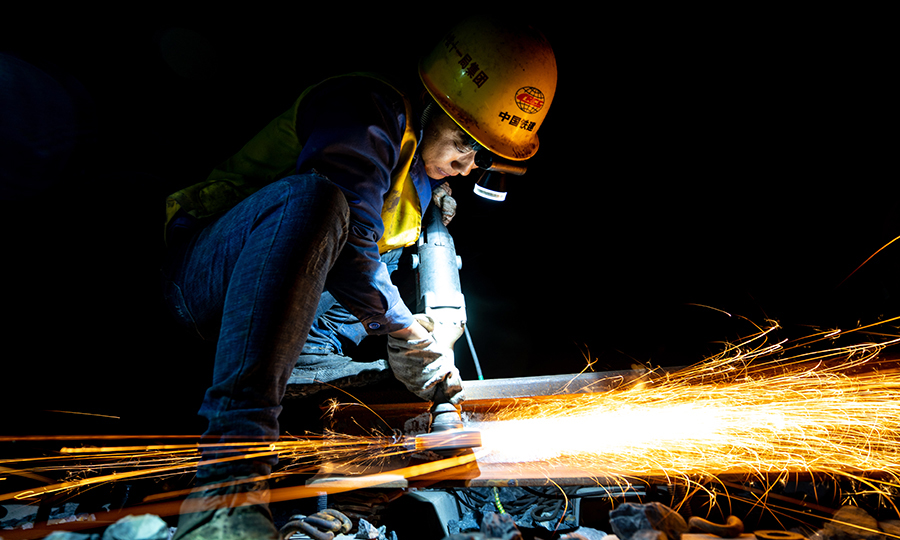 在400多公里的拉林鐵路線上，高寒缺氧、晝夜溫差大，如何保證全線無縫焊接的質量？有這樣一群夜行者，他們用晝伏夜出的工作方式給了我們答案。白天鋼軌溫度達到了60攝氏度，為保證“應力放散鎖定”工序的質量，他們通常晚上9點等軌溫降下來了才開始工作，為了不耽誤第二天施工運輸車輛的通行，凌晨5點就匆匆下班。他們手里握著的不僅僅是900攝氏度的鋼軌更是藏族同胞的信任與期盼。圖為工人正在進行除銹作業。（丁慶濱 攝）