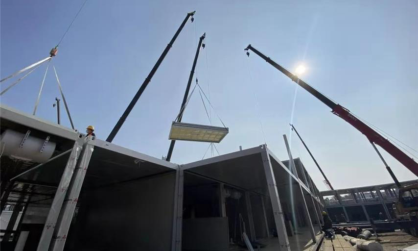 截至1月30日中午12時，武漢火神山醫院項目場地平整、砂石回填、HDPE膜鋪設全部完成，基礎混凝土澆筑完成95％；集裝箱板房進場、改裝、吊裝正快速推進。管線溝槽開挖、埋設級回填完成50％；污水處理間設備吊裝完成，管道安裝完成60％；調蓄水池HDPE膜開始鋪設。圖為住院樓板房吊裝現場。