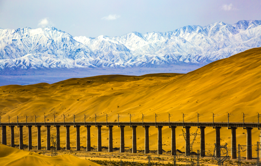 自2012年底敦格鐵路開工建設以來，中國鐵建科學組織、優化施工方案、合理安排作業時間，先后順利完成了全線多個重點控制性工程施工。在當金山隧道施工中，建設者大力進行科技創新，攻克高寒缺氧等難題，創造了我國隧道獨頭掘進最長、高原隧道施工通風距離最長的紀錄。圖為沙山溝特大橋與沙山、雪山融為一體，美輪美奐。（金偉 攝）