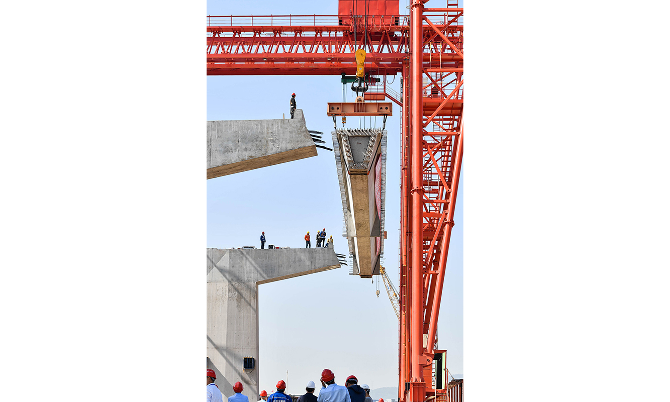 在建的深中通道是集“橋、島、隧、水下互通”于一體的跨海集群工程，全長約24公里，包括6.8公里海底隧道和17.5公里跨海橋梁。深中通道建成通車后，將成為連接珠江東西岸的重要通道，屆時兩地間通勤時間將由兩小時縮減至30分鐘。圖為11月21日，中鐵大橋局施工人員在中山市翠亨新區架設深中通道首片箱梁。（新華社記者 劉大偉 攝）