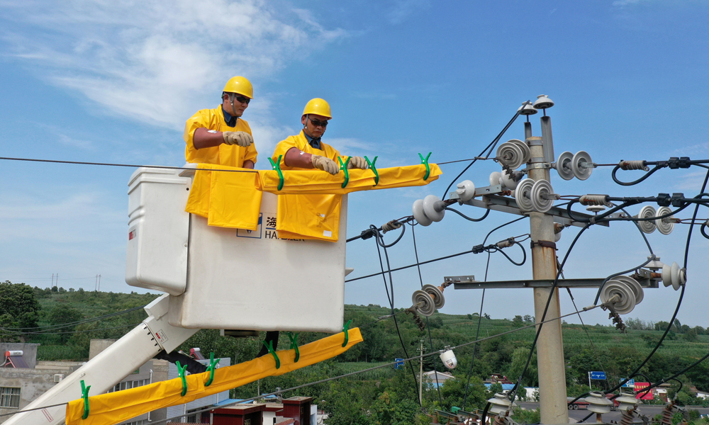 帶電作業是在高壓設備上不停電進行檢修、測試的一種作業方法，盛夏酷暑是帶電作業最頻繁的時候，尤寧和隊友穿著絕緣服裝，高溫下作業異常辛苦。圖為7月30日，在河南省新安縣正村鎮上坡村，尤寧（左）和同事進行帶電作業。（新華社記者 馮大鵬 攝）