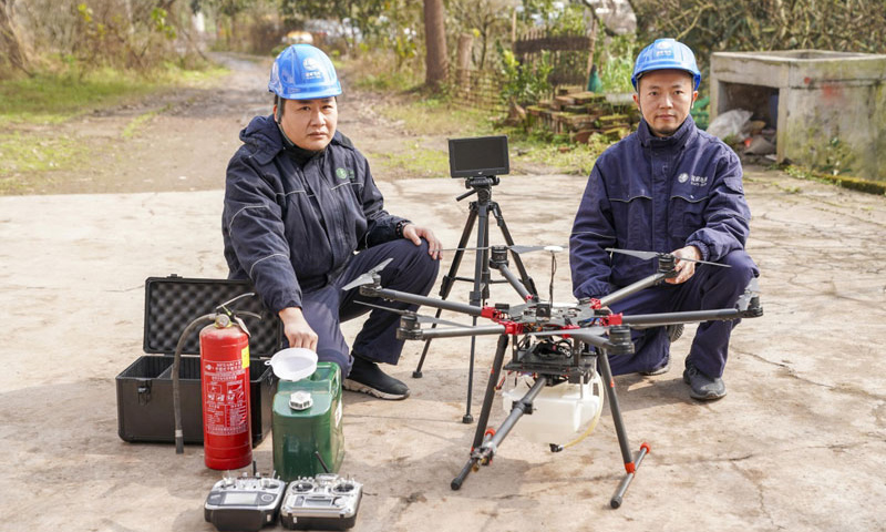 這臺多旋翼無人機，通過搭載帶有燃料箱、油泵、自動點火裝置的噴火吊艙任務模塊，可以對影響高空電力線路安全的飄掛物進行定點障礙清除作業。圖為噴火清障無人機的研發負責人何濤（右）和同事晏新展示噴火清障無人機。（新華社記者 劉潺 攝）