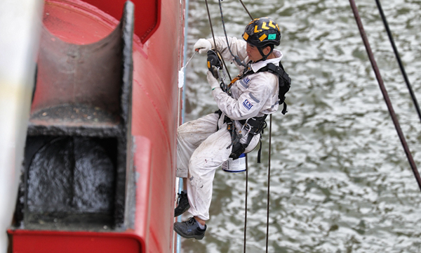 圖為工作人員利用鋼鐵繩索下至船舷外部，進行涂裝作業。（李豫黔 攝）