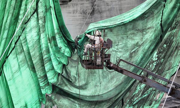 在實施船體外部打砂作業前，工作人員先用隔離布將船體包住，有效阻擋了作業過程中的銅礦砂粉塵外泄，減少了對環境的影響。（李豫黔 攝）