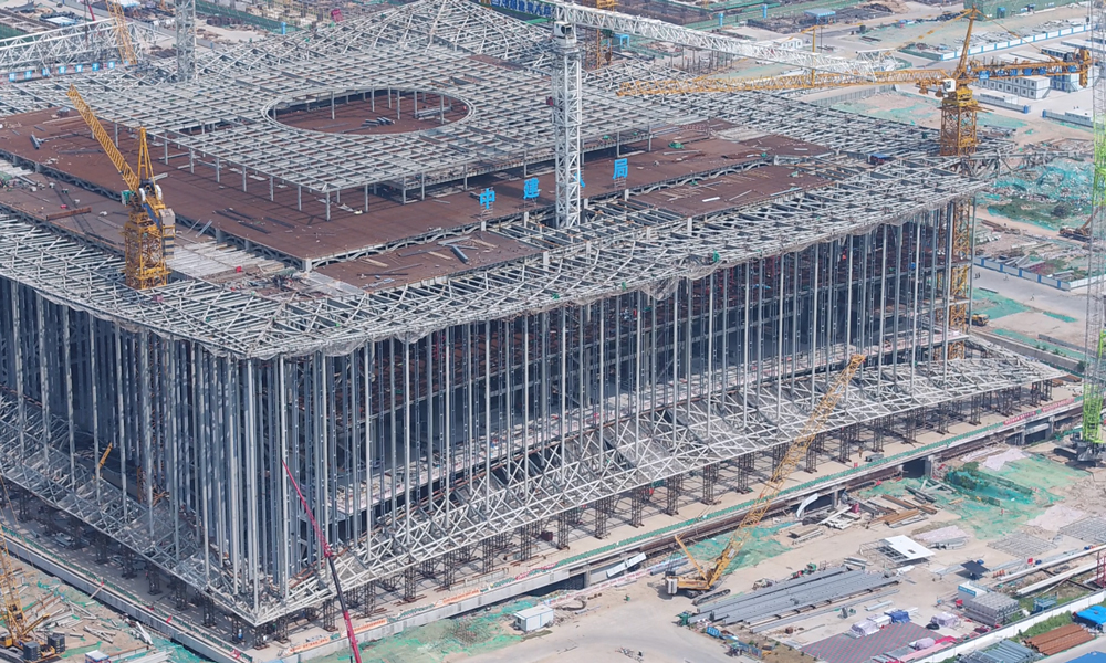 西安絲路國際會議中心選用核心筒+桁架的懸掛結構體系，創造了特有的無柱空間體驗。在建筑外部，屋頂桁架懸掛下來的180根白色鋼柱（柱高45-30米，直徑0.6米）和上下兩個白色“月牙”以線與面的方式相互呼應。圖為施工人員正在對上月牙鋁板進行整體吊裝。（北京電視臺 劉通 攝）