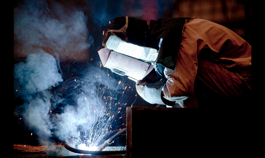 盡管室外氣溫已達38攝氏度，因為安全防護需要，中鐵四局鋼結構建筑公司制造分公司的作業工人也必須把自己從頭到腳防護起來。汗水從帽子和眼鏡的縫隙里流淌下來。每個工位都有不停轉的風扇，每個工人都有超大容量的水杯。每年他們都要經歷百十來個這樣難熬的高溫工作日。（作者：朱曉晨）