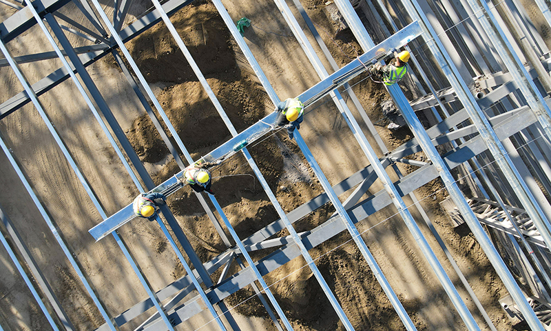 工人在20余米高的新疆塔城重點開發開放試驗區一處風機葉片制造項目頂部進行屋面檁條安裝作業（5月18日無人機拍攝）。新華社記者 高晗 攝