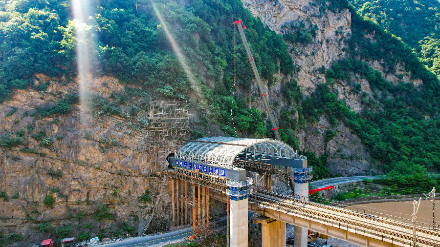 該工程位于甘肅省天水市與陜西省寶雞市交界處，上跨隴海鐵路與G310國道。該柔性鋼棚洞由長寬各24米、重65噸的鋼棚架以及兩條各長37米、重113噸的縱梁構成。隧洞與既有隧道凈空距離僅3米，圍巖硬度高，且位于陡峭邊坡上。施工空間窄、時間緊、風險高、難度較大。圖為安裝成型后的鋼棚洞。