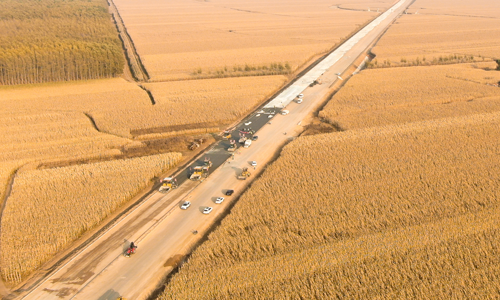 在田間地頭，農民們忙著收玉米，將一年的勞動成果打包帶回家；在施工現場，建設者們揮汗如雨，全面加快路面施工。長太高速公路是吉林省中西部地區的一條重要干線通道，整條線路穿過著名的“黃金玉米帶”、我國大型商品糧和油料基地，并輻射內蒙古東部通遼市、興安盟等多個旗縣。圖為長太高速沿路布滿玉米田。