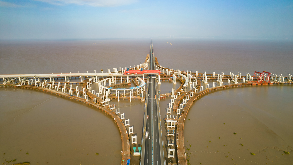 杭甬高速復線寧波一期工程全長55.833千米，為雙向六車道高速公路標準，設計時速120千米。該工程主線橋在寧波市鎮海區一跨直接越過甬舟高速金塘大橋，并設濱海互通與金塘大橋相接，主線橋箱梁梁底與金塘大橋橋面凈空約7.6米，海上架梁施工安全風險極高，為全線唯一一處Ⅳ級施工風險點。圖為濱海互通主線橋跨越金塘大橋架梁現場。