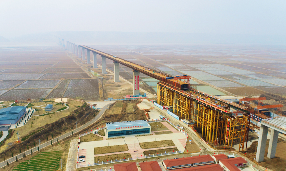 臨猗黃河大橋位于山西省運城市臨猗縣內，橫跨山西陜西兩省，是國家高速公路菏寶線G3511的控制性節點工程，大橋全長5427米。采用大跨度整幅橋核心箱組合梁步履式頂推工藝施工，基本跨徑為128米，鋼梁總重5.7萬噸，連續頂推重量2.9萬噸，頂推精度要求高、施工難度大。圖為大橋山西側施工作業現場。