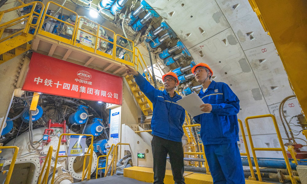 針對工程特點和項目需求，中鐵十四局對盾構機進行了針對性設計優化，聯合研發了具有自主知識產權的“新穿越號”盾構機，配置高承壓主驅動密封、大流量泥水沖刷環流系統、高效物料運輸及智能化預制構件同步拼裝技術、壁后同步注漿密實度檢測系統等多項關鍵技術，大幅度提高盾構機的適應性和可靠性，為工程順利實施保駕護航。圖為技術人員正在檢查“新穿越號”盾構機的掘進狀態。