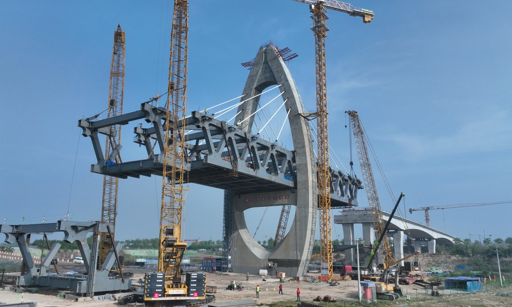 作為國家“十四五”期間重點推進的150項重大水利工程之一，引漢濟渭二期工程由黃池溝配水樞紐、南干線工程和北干線工程三部分組成，線路全長190公里，其中北干線輸水管道渭河管橋全長1.23公里，是引漢濟渭二期工程最大單體項目和控制性工程，也是國內水利領域首座四塔五跨鋼桁梁斜拉結構的特大橋。大橋主橋采用鋼結構設計，由四座索塔和48對斜拉索組成，索塔高度73.5米，橫跨渭河主河道，設計采用水滴造型，美觀獨特，工藝復雜，施工難度大。圖為鋼桁梁標準節吊裝現場。