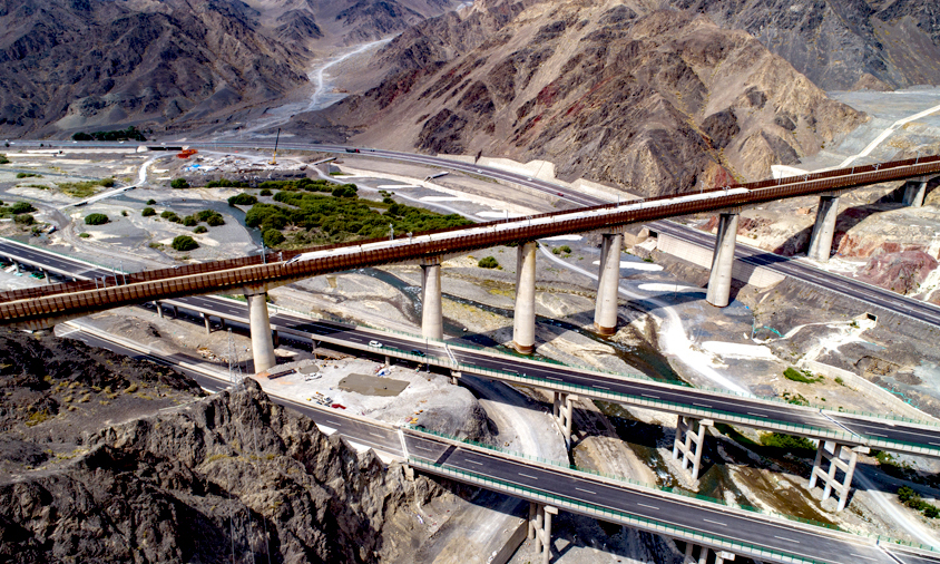 連霍高速公路起于連云港，止于霍爾果斯，全長4395千米，是“一帶一路”重要交通大動脈，中國最長的高速公路。小烏段橫跨亞洲最大的風力發電站，穿越天山山脈，建設者克服常年大風、低溫天氣及復雜的地質條件，如期完成上行線通車任務。圖為連霍高速下穿蘭新高鐵。