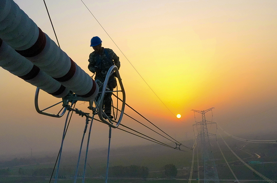在停電前，項目組織人員提前在地面整體組立重達70多噸的鐵塔，然后再進行整體吊裝，將工效提高了20%，順利完成遷改任務。圖為夕陽中的電力施工工人。（范成濤 攝）
