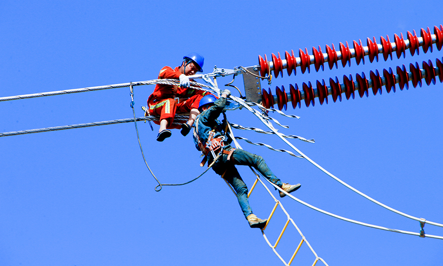 濟萊高鐵與城鵬線有三處交叉，為保障高壓電力線路遷改安全，在既有線處遷改施工時，采用鐵路上空鋪設絕緣防護網的施工方案，以確保下方列車安全運行。圖為工人用軟梯在高空中施工。（范成濤 攝）