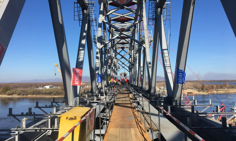 同江中俄鐵路大橋工程于2014年2月26日奠基，是中俄首座跨界河鐵路大橋，設計鐵路年過貨能力2100萬噸。大橋全長7193.71米，其中跨江大橋主橋全長2215.02米，中方境內1886.45米，俄方境內328.57米。圖為10月13日，同江中俄鐵路大橋中方最后一吊鋼梁安裝到位。（新華社記者 王君寶 攝）