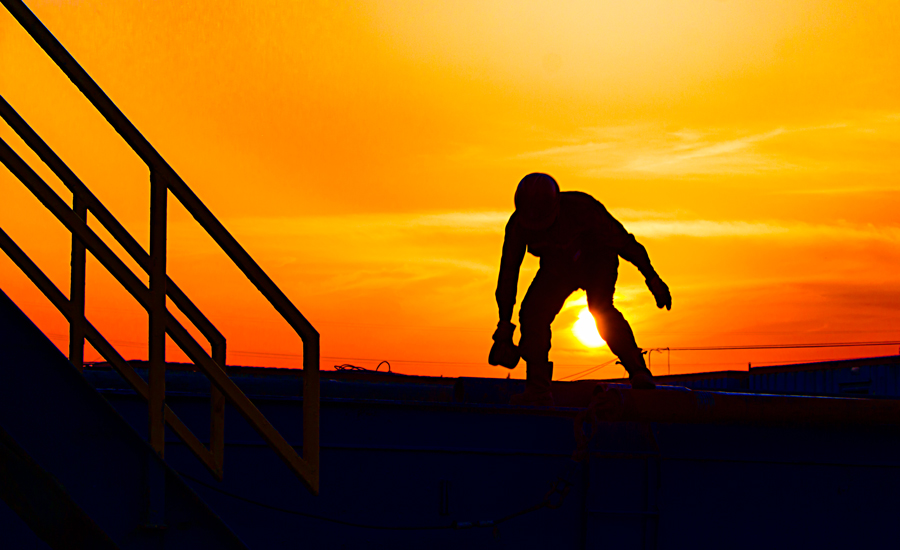 2017年5月28日，夕陽西下，湖北省潛江市江漢油田五七一鉆井隊，一名鉆井工正在鉆桿上檢查鉆桿質量，為下鉆做準備。（作者：曾黎紅）